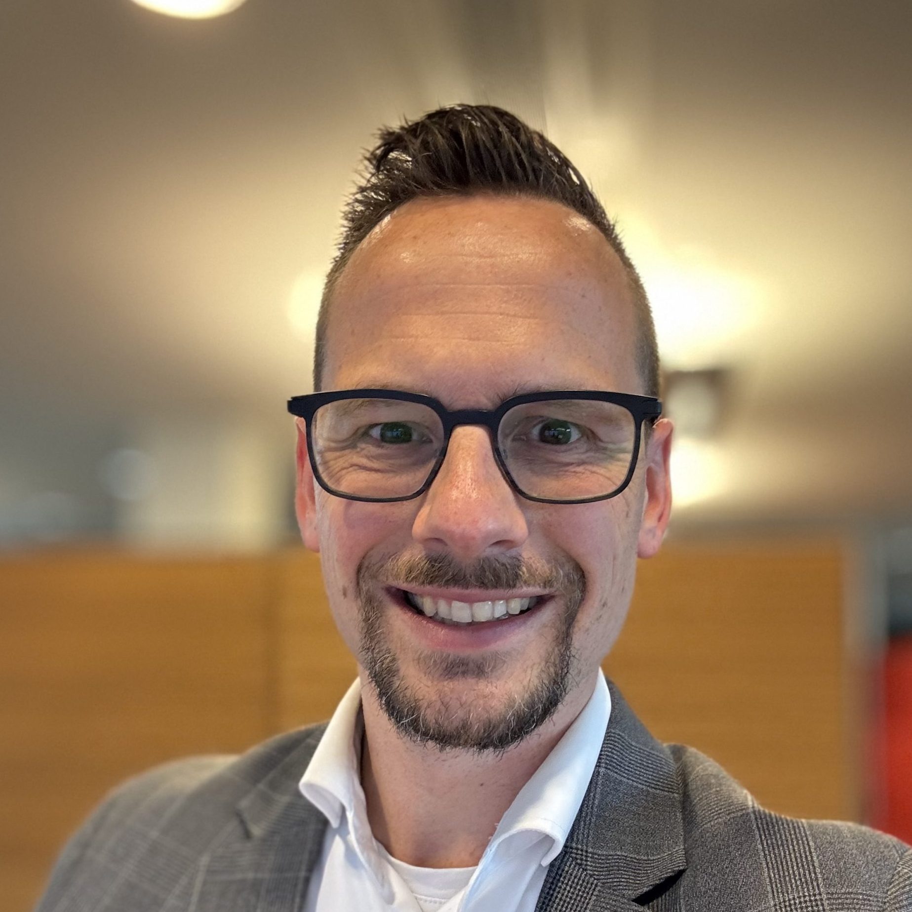 Michiel Haagen, man 40 jaar, met bril. Kort haar, ringbaardje en een grijs jasje met wit overhemd.