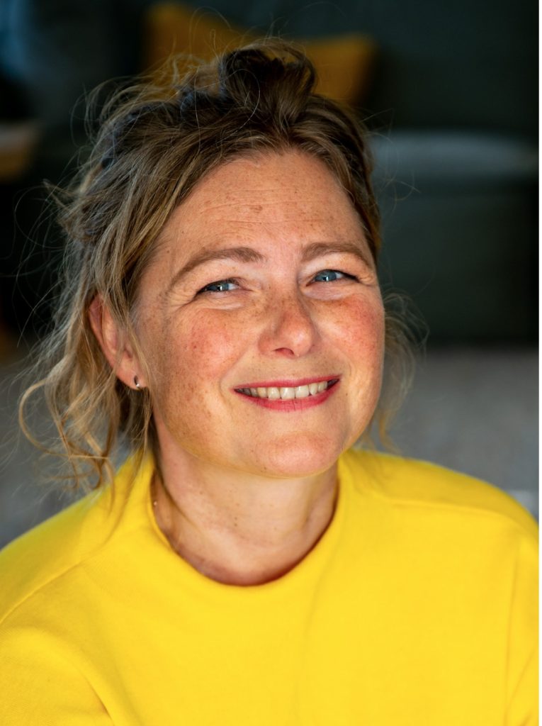 Ingrid Pfrommer, blauwe ogen, gele trui, donkerblond haar lang haar.
